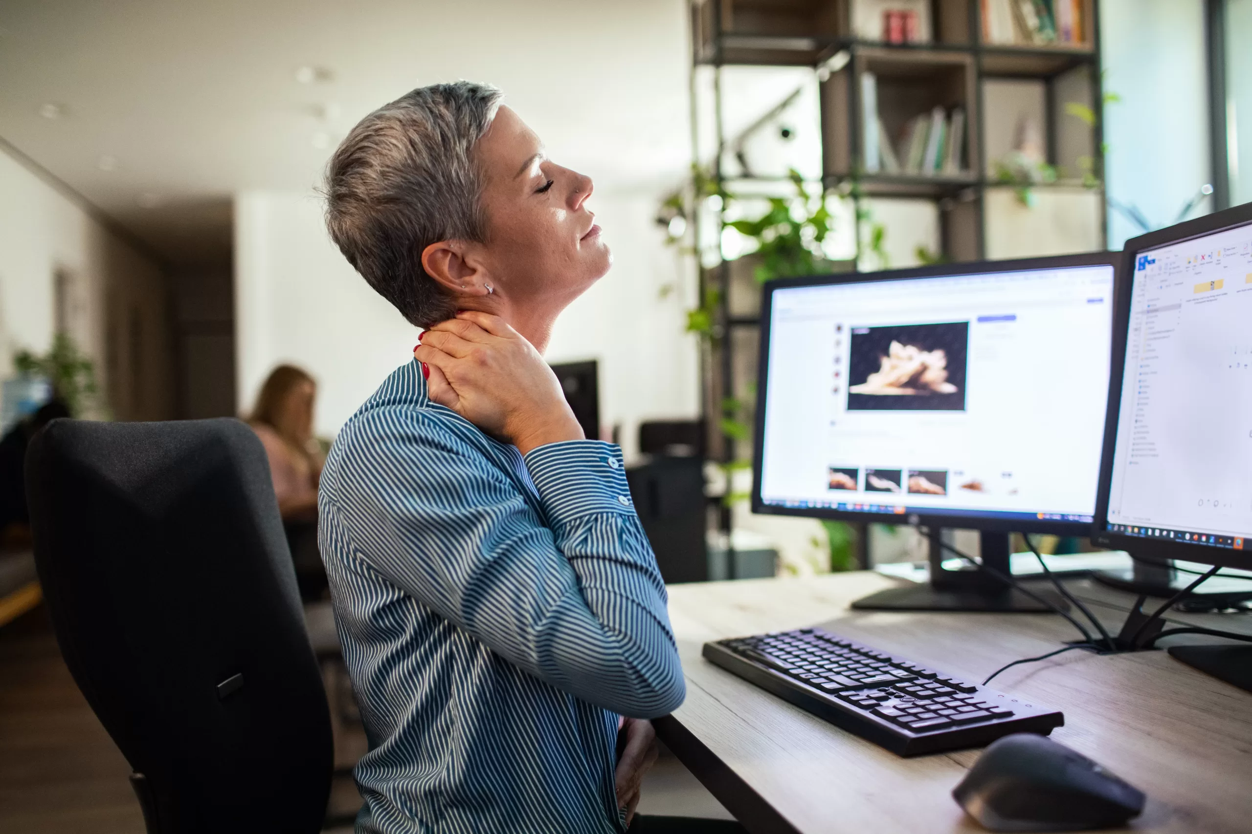 Occupational Health provision for SMEs - A female gabbing the back of her neck with her hand sitting at a work desk