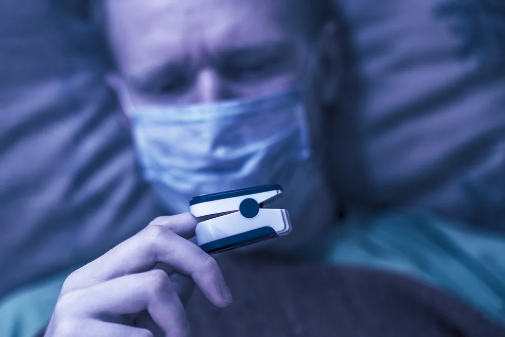 Reducing employee absence - Picture of man in bed with facemask and blood temp gauge on finger
